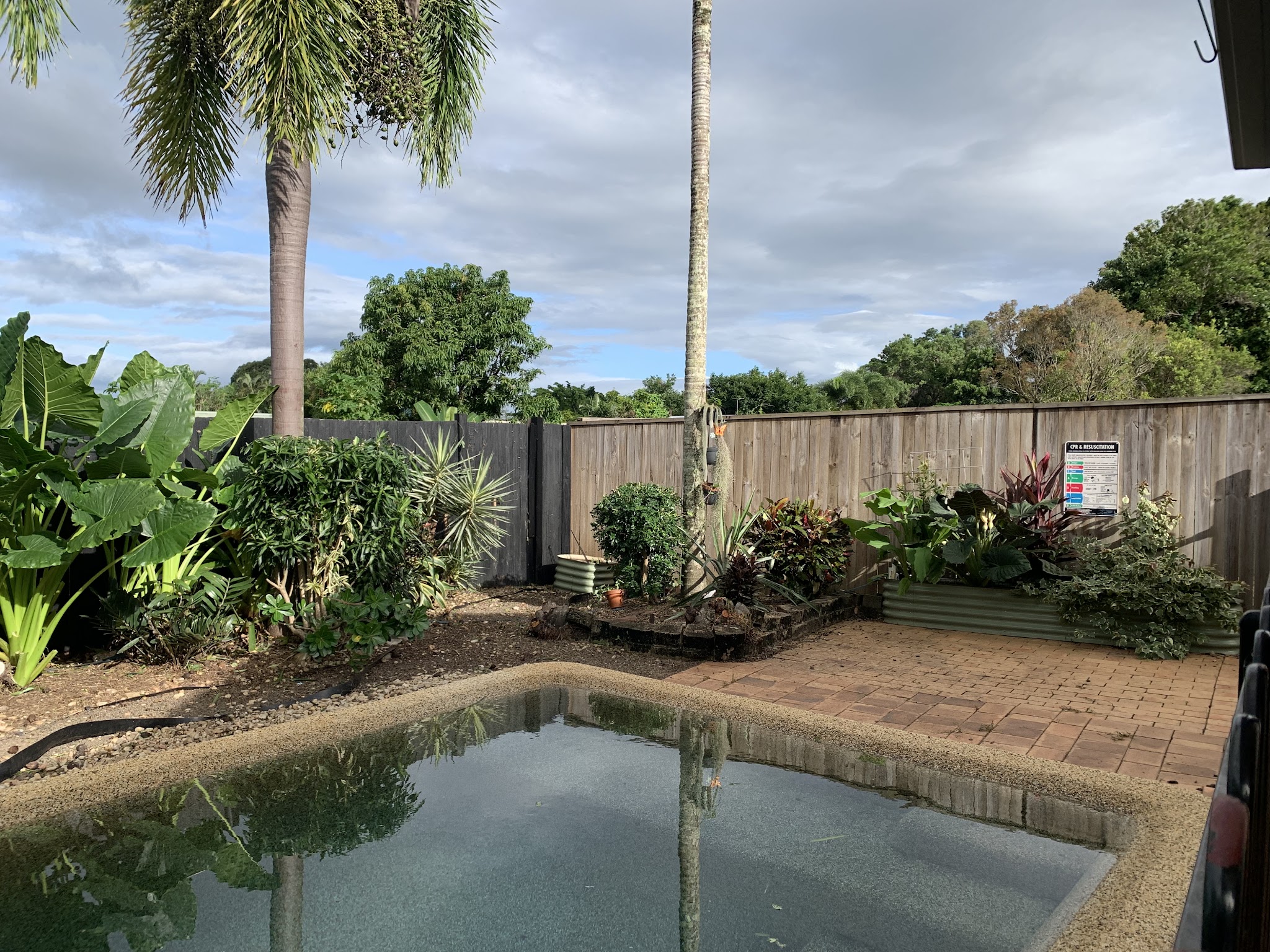 The same pool surround tidied, with defined beds, swept brick paving and a raised Colorbond garden bed