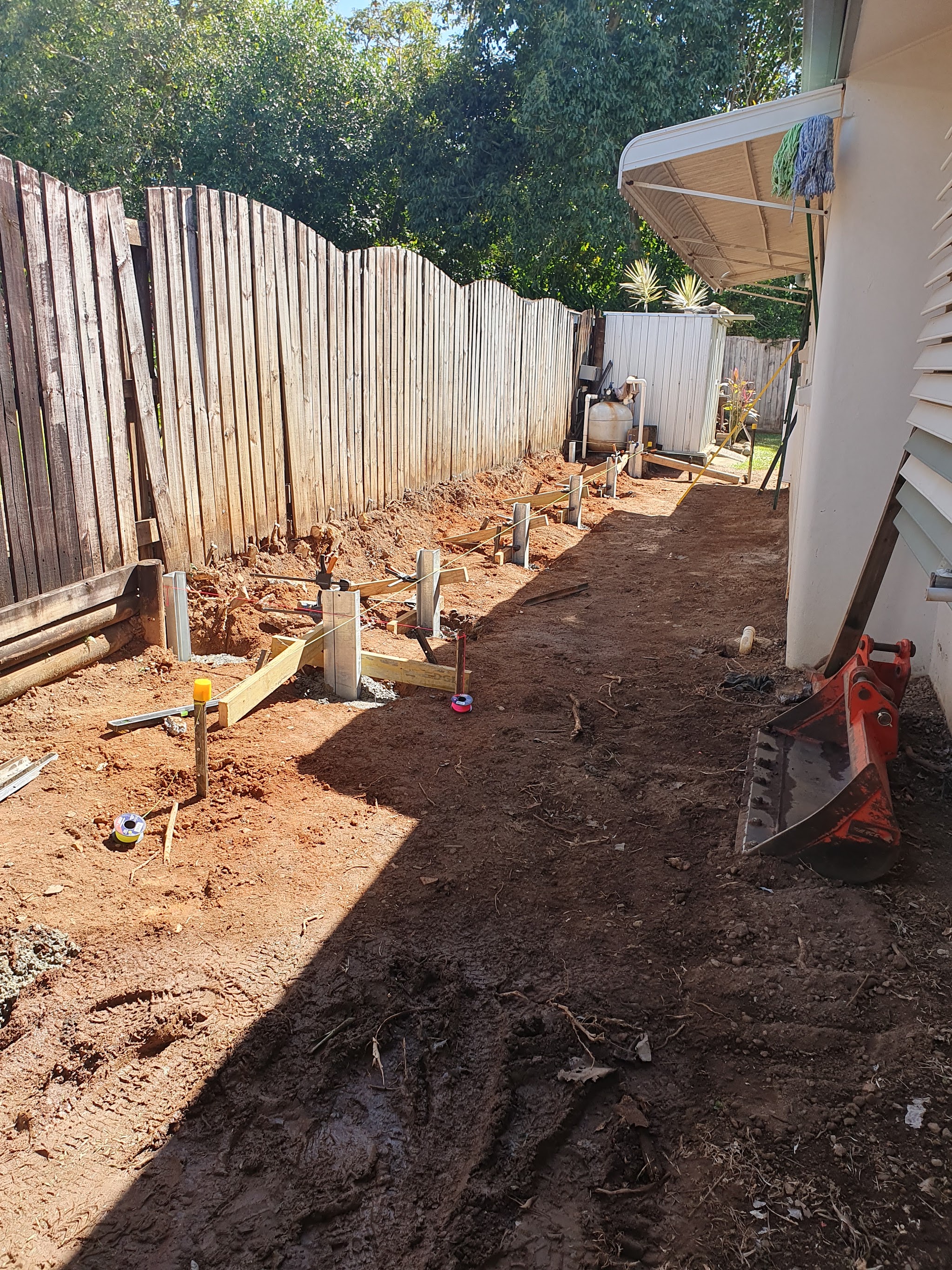 The side path excavated back to red soil, with string lines set and galvanised posts and sleepers going in for a new retaining wall